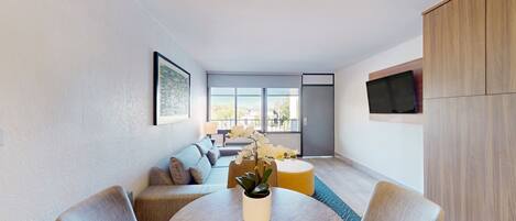 A modern living room with a round dining table, a sofa, and a TV mounted on the wall.