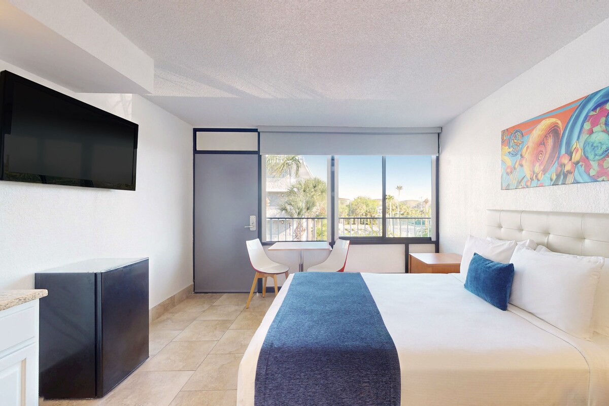 A hotel room with a bed, a desk, a chair, a TV, and a balcony with a view.