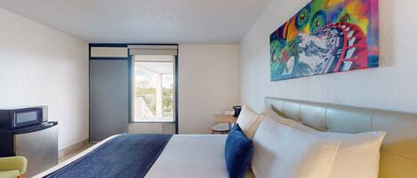 Una habitación de hotel con cama, escritorio, silla, un cuadro y ventana.