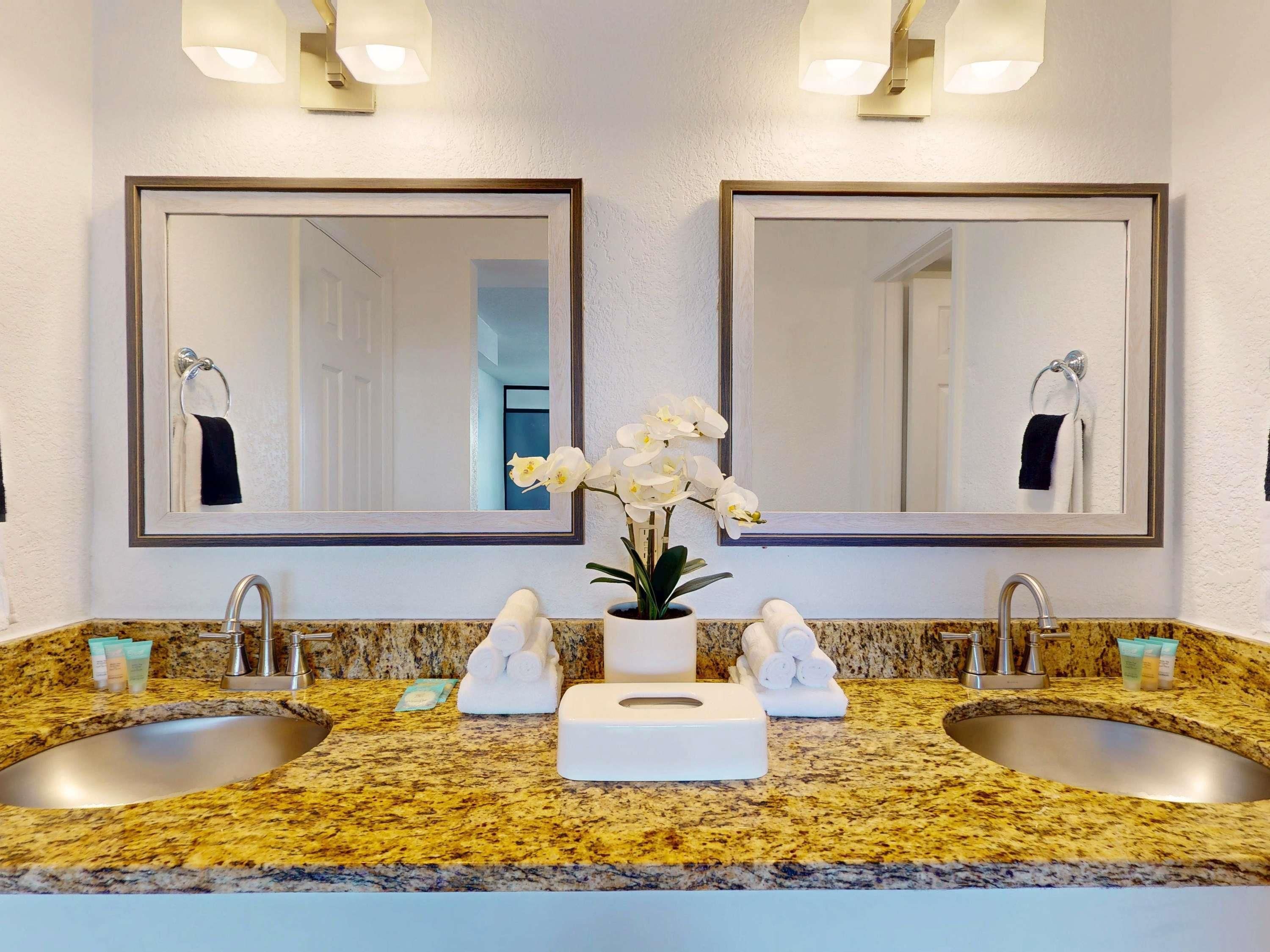 A bathroom with two sinks, a mirror, and a vase with white flowers.
