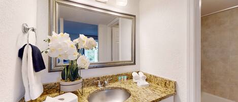A bathroom with a granite countertop, a sink, a toilet, a mirror, and a vase with white flowers.