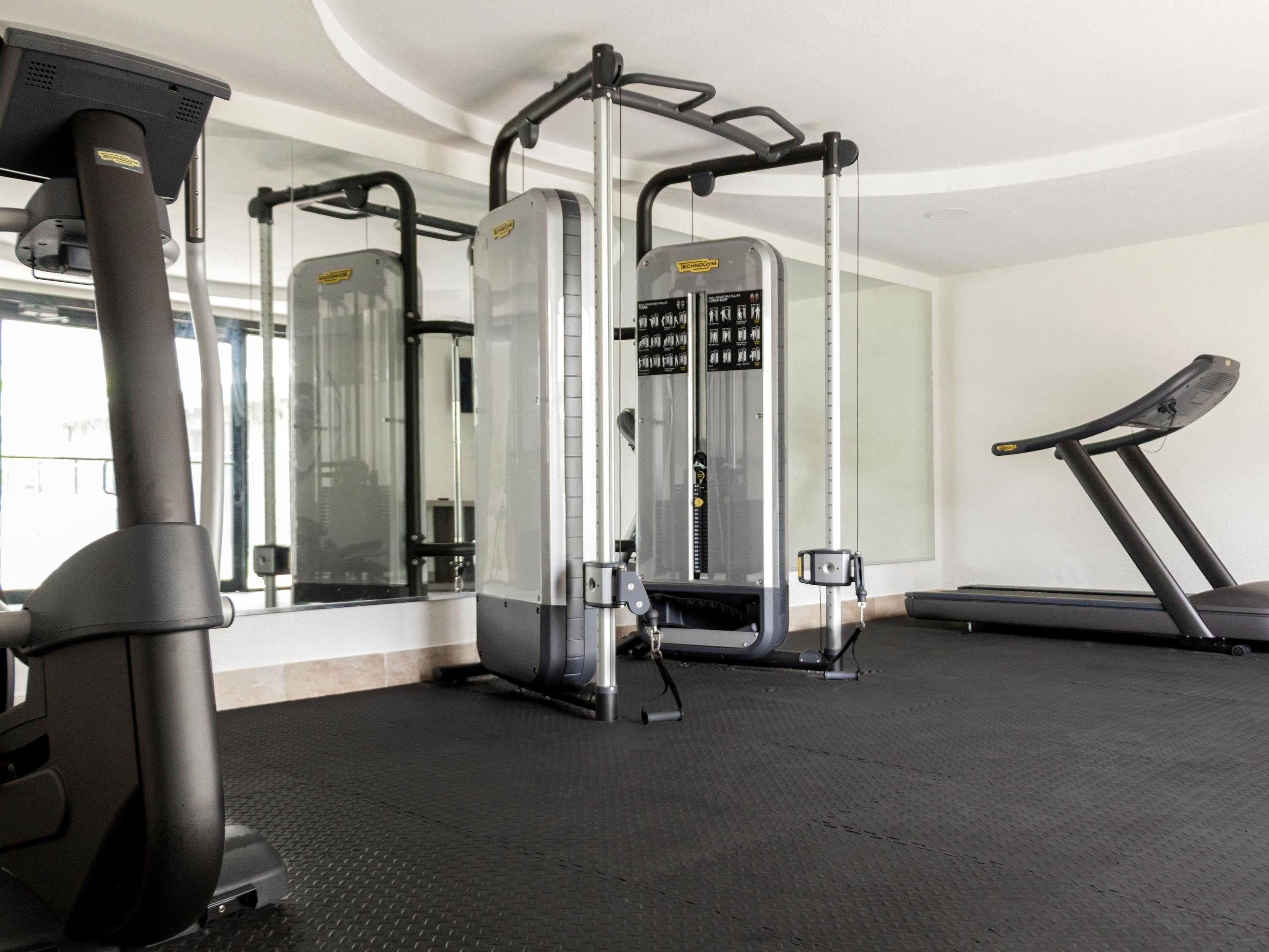 Une salle de sport équipée d’un tapis de course, d’appareils de musculation et d’un mur recouvert de miroirs.