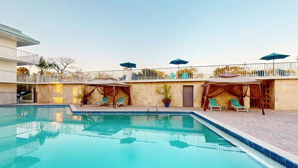 A swimming pool with lounge chairs and umbrellas, surrounded by a stone wall and a balcony with railings. - Park Royal Orlando managed by Accor (Kissimmee)