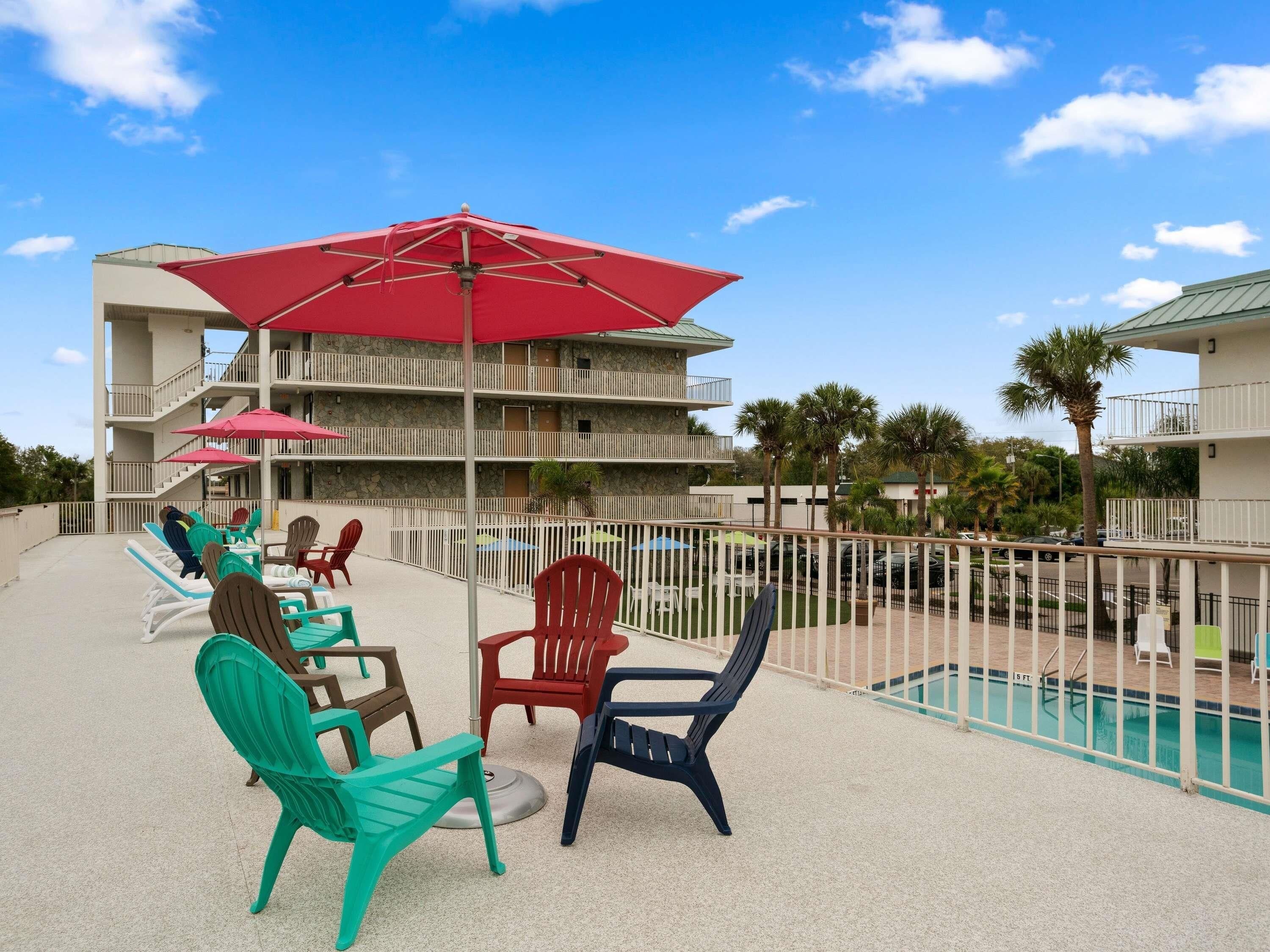 A poolside area with lounge chairs and umbrellas, a pool, and a multi-story building with balconies.