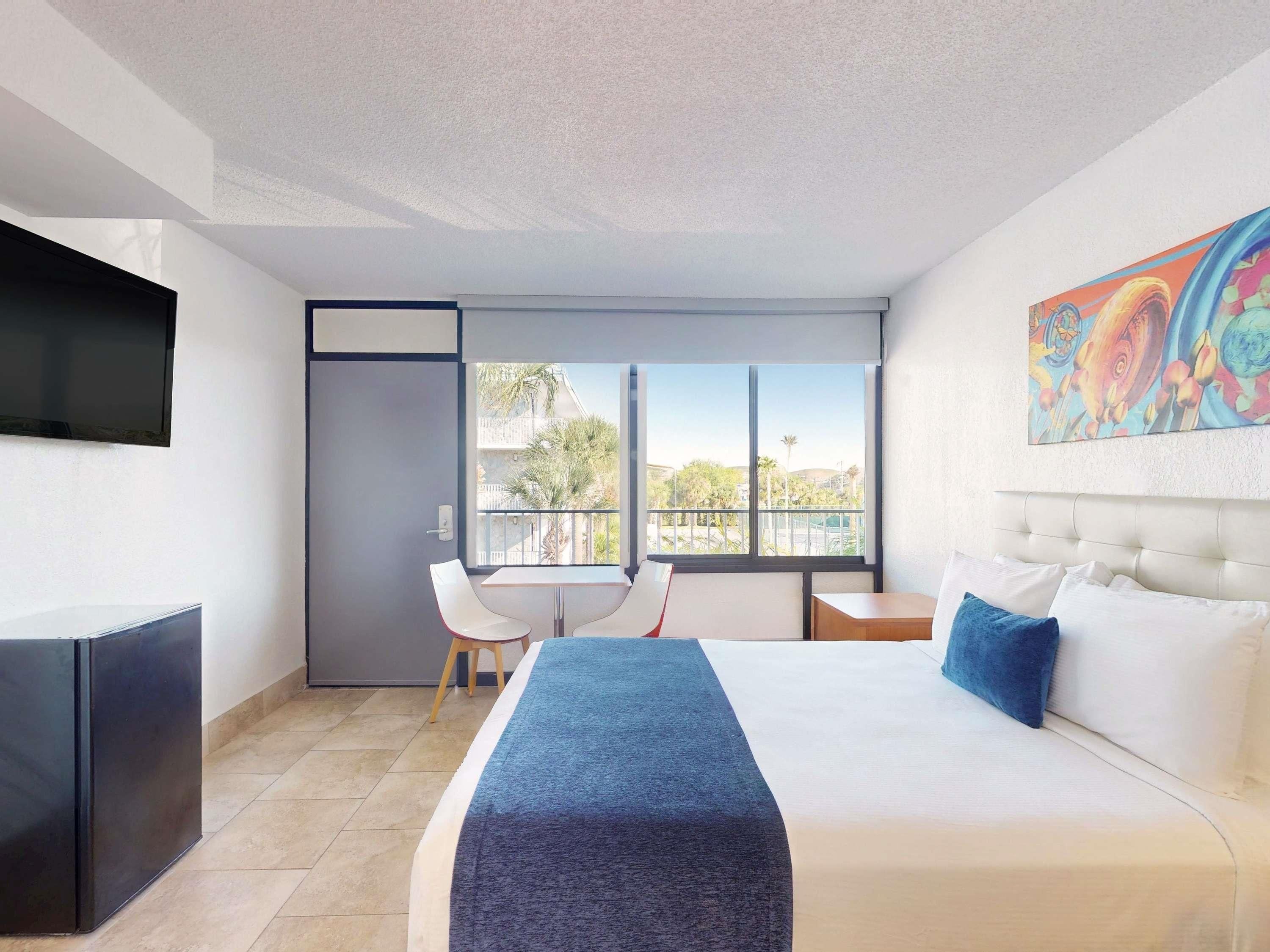 Ein Hotelzimmer mit Bett, Schreibtisch, Stuhl, Fernseher und einem Balkon mit Blick.