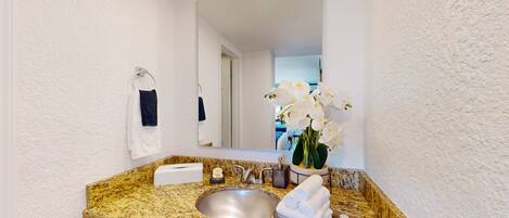 A bathroom with a granite countertop, a sink, a mirror, a towel rack, and a vase with white flowers.