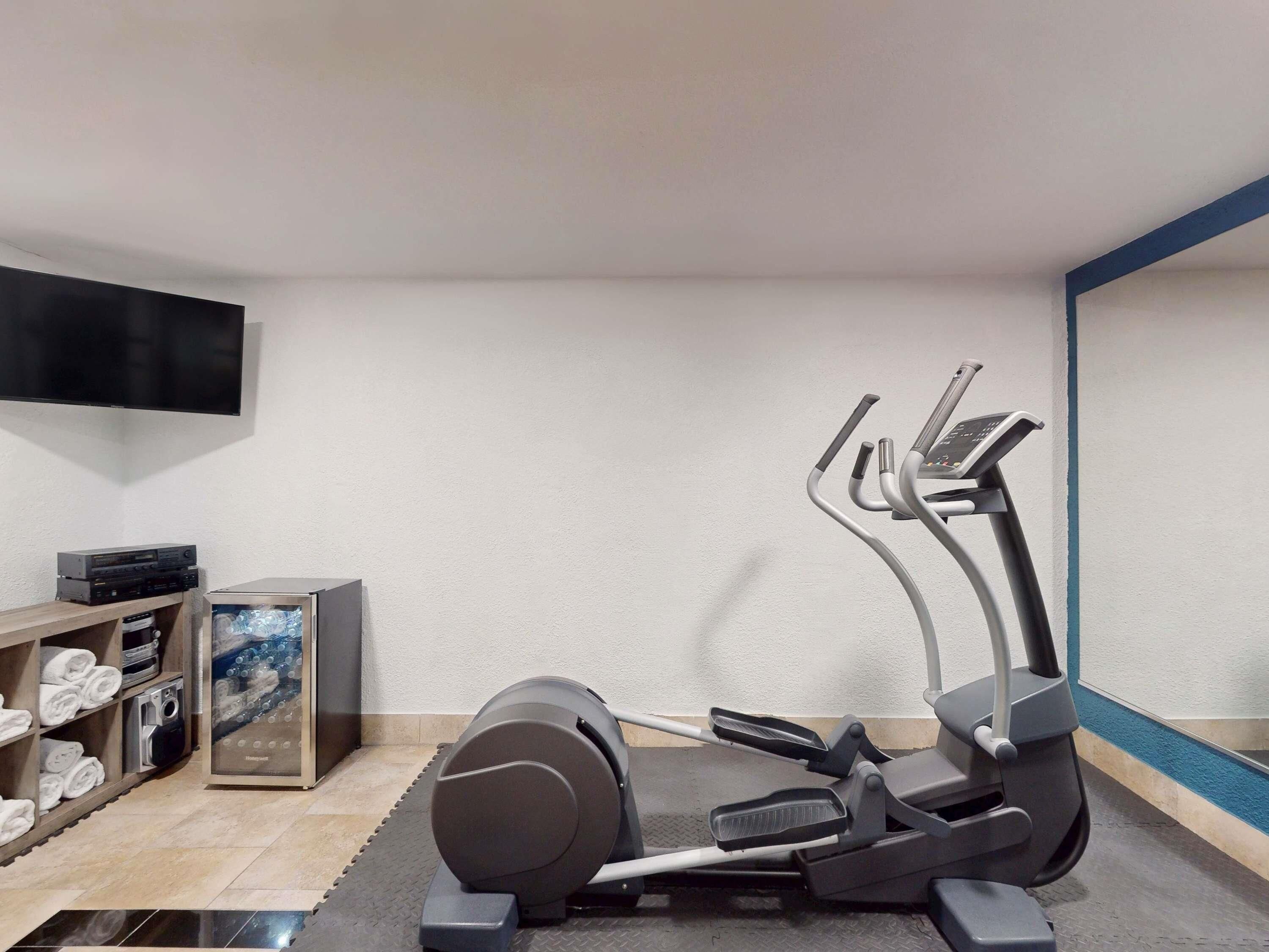 Un gimnasio en casa con una máquina elíptica, un televisor y un reproductor de DVD en un estante.