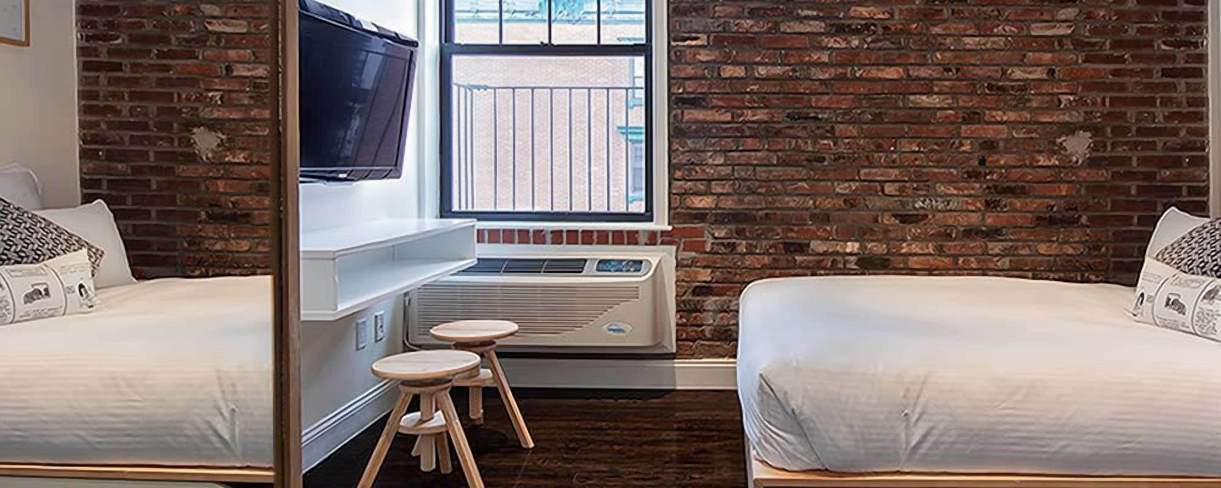 A room with two beds, a TV, a window, and a brick wall.
