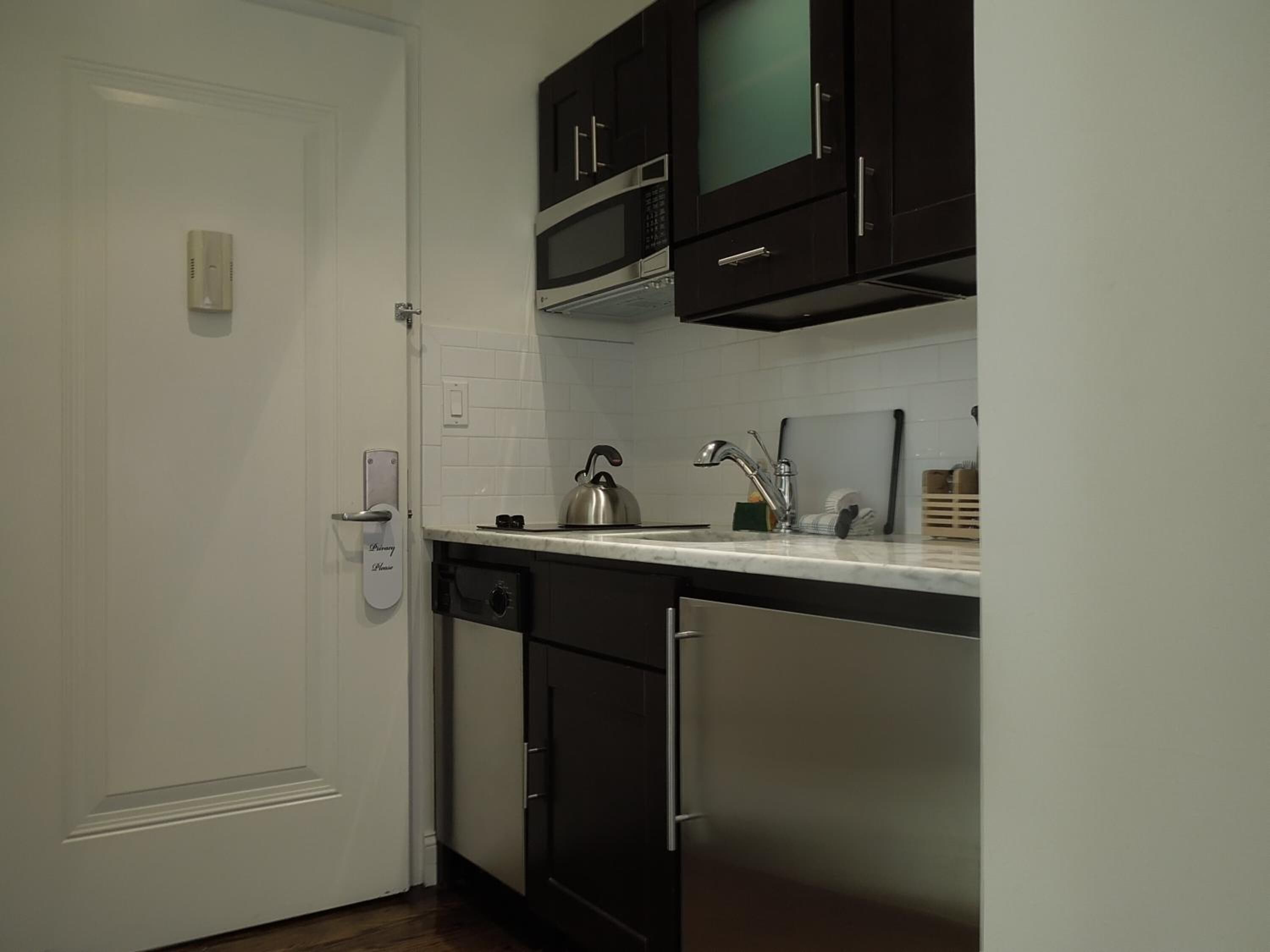 A compact kitchen with dark cabinets, a white countertop, and a stainless steel kettle.
