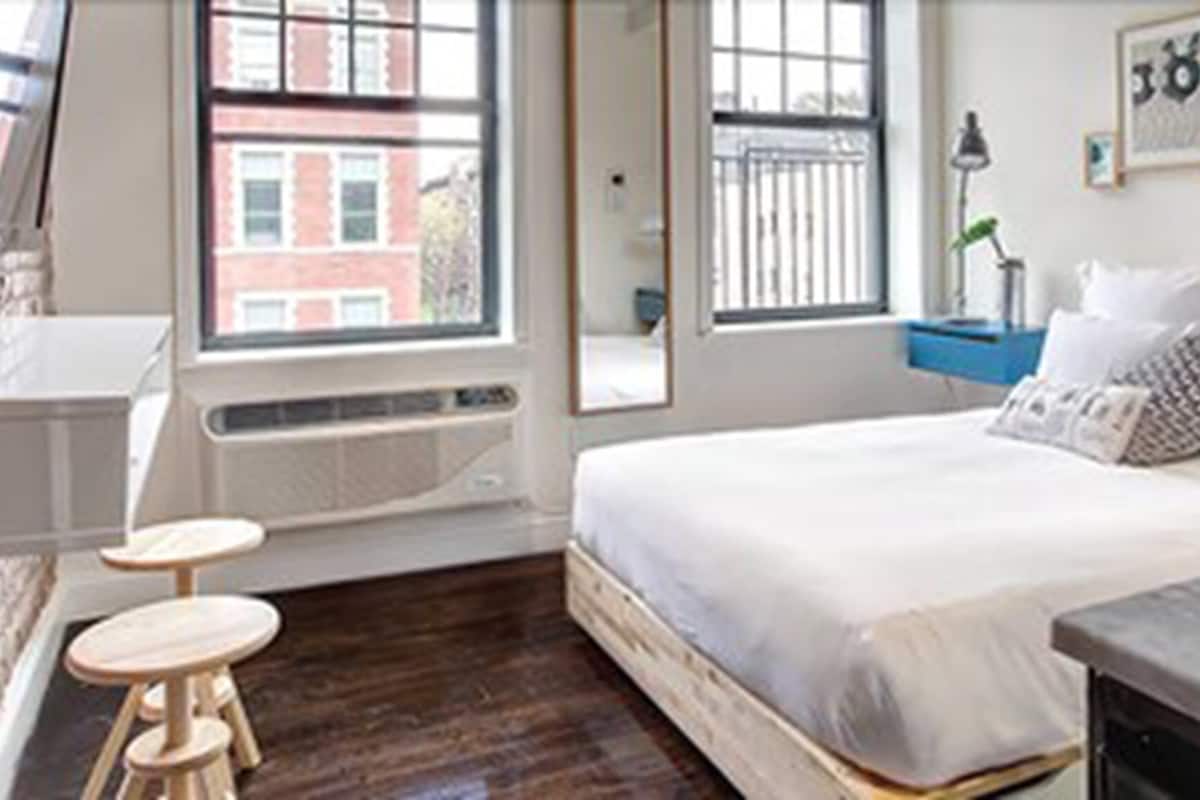 A bedroom with a bed, a small table, a window, and a stove.