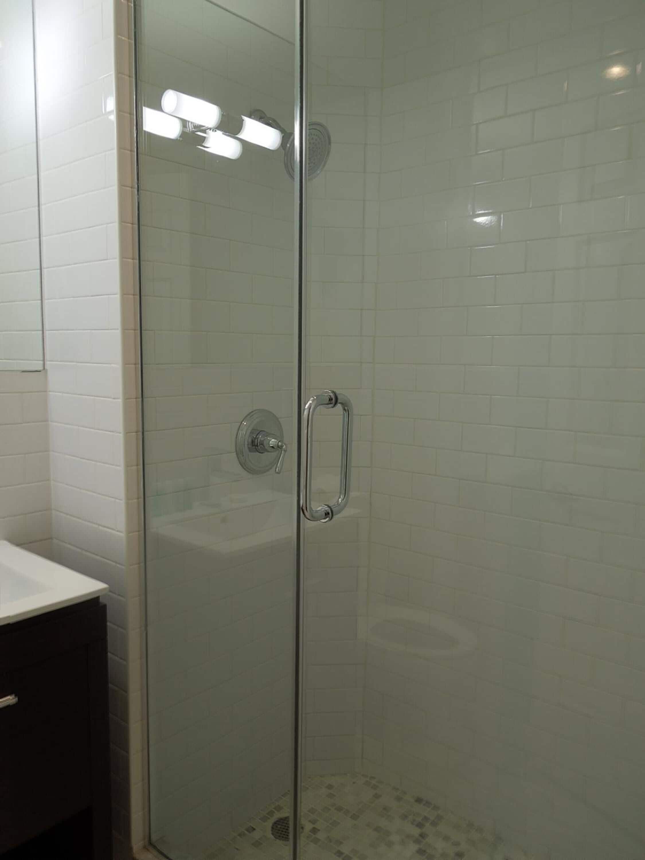 A glass-enclosed shower with a chrome handle and a white tiled wall.
