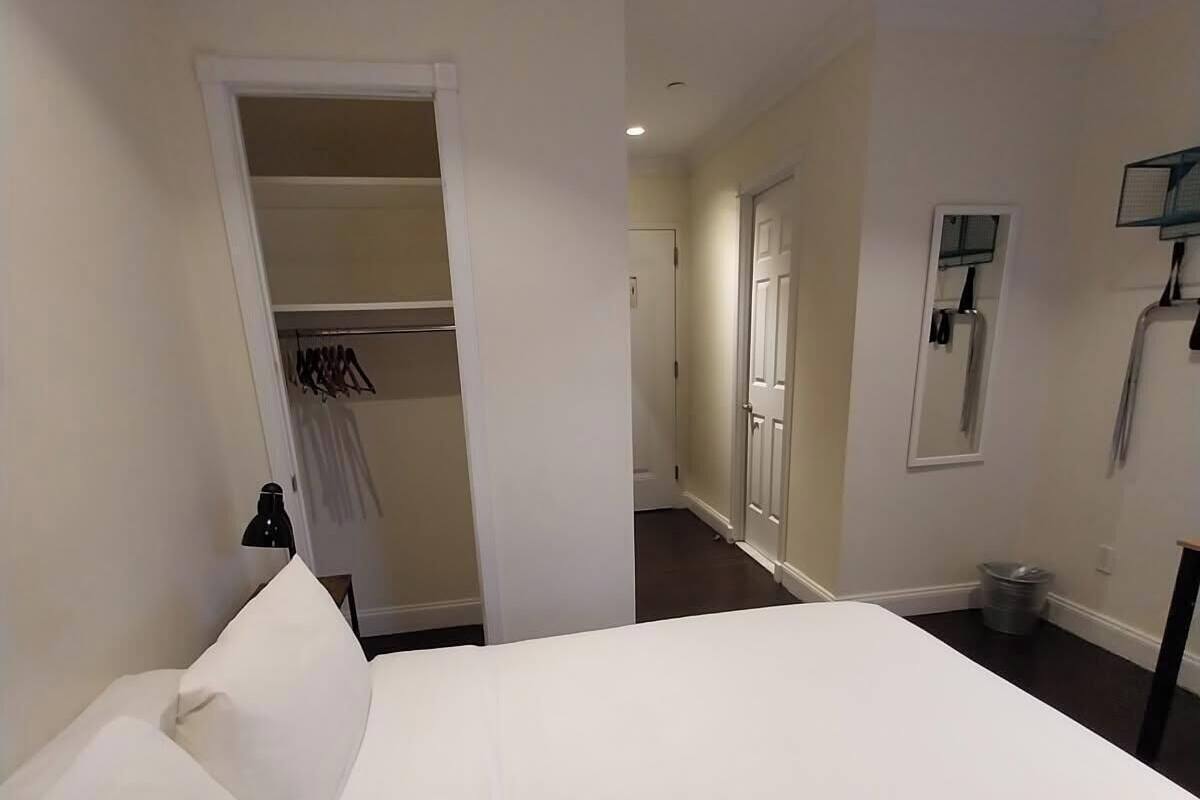 A hotel room with a bed, a closet, a bathroom with a mirror, and a hallway.