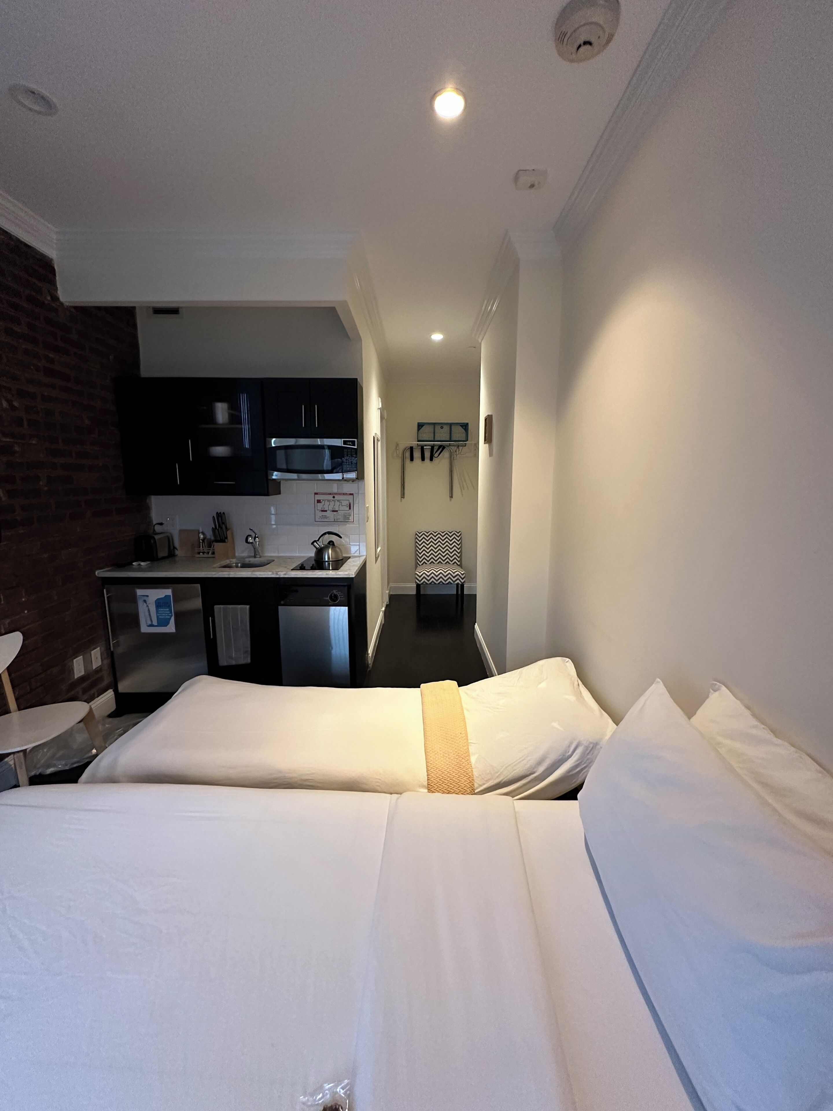 A hotel room with two beds, a kitchenette, and a small bathroom.