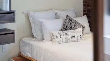 A bedroom with a bed, a nightstand, a drawer, a potted plant, and a framed picture on the wall.