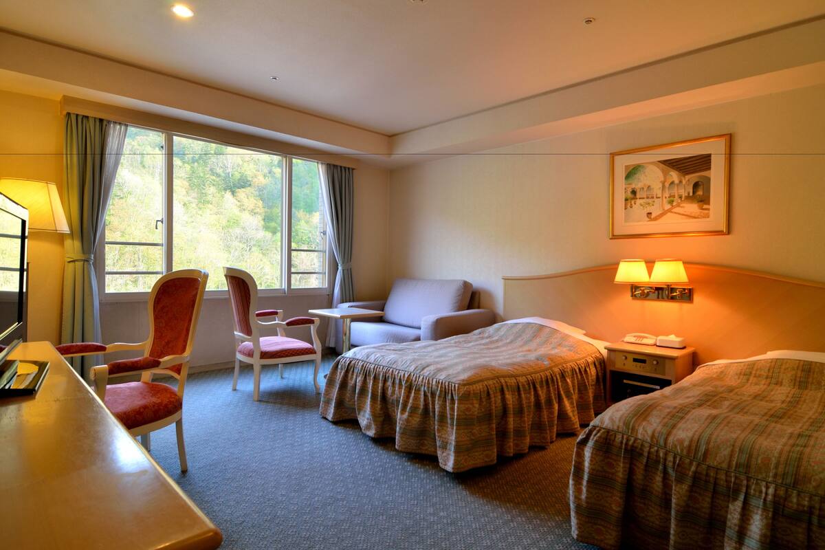 Ein Hotelzimmer mit zwei Betten, einem Schreibtisch, einem Stuhl, einem kleinen Tisch und einer Lampe.
