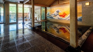 Un onsen japonés tradicional con un amplio mural de piedra, vigas de madera y piso de baldosas.