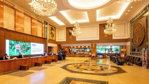 Un lobby espacioso con techo alto, candelabros ornamentales, una pantalla digital grande y un mostrador de recepción.