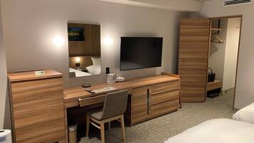 A hotel room with a wooden desk, a chair, a bed, a TV, and a wardrobe.