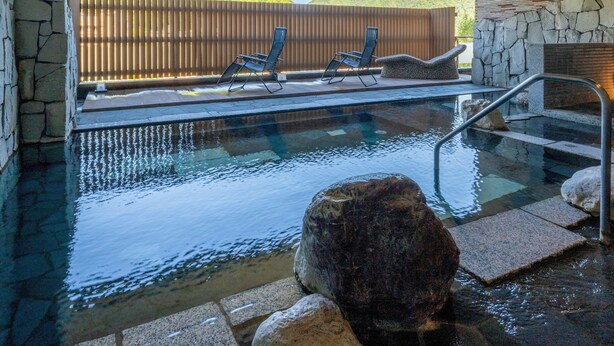 Un área de piscina interior con paredes de piedra, un muelle de madera y sillones de descanso.