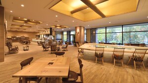 Un amplio comedor interior con mesas y sillas de madera, ventanas grandes y un techo alto con vigas a la vista.