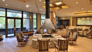 Un espacio interior amplio con una chimenea grande, muebles de madera y ventanas grandes que ofrecen vistas del exterior.