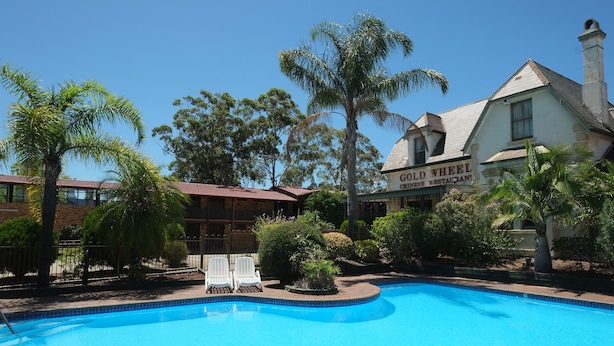 A swimming pool with lounge chairs, a building labeled "Gold Wheel Country Restaurant," and surrounding greenery. - Maclin Lodge Motel (Campbelltown)
