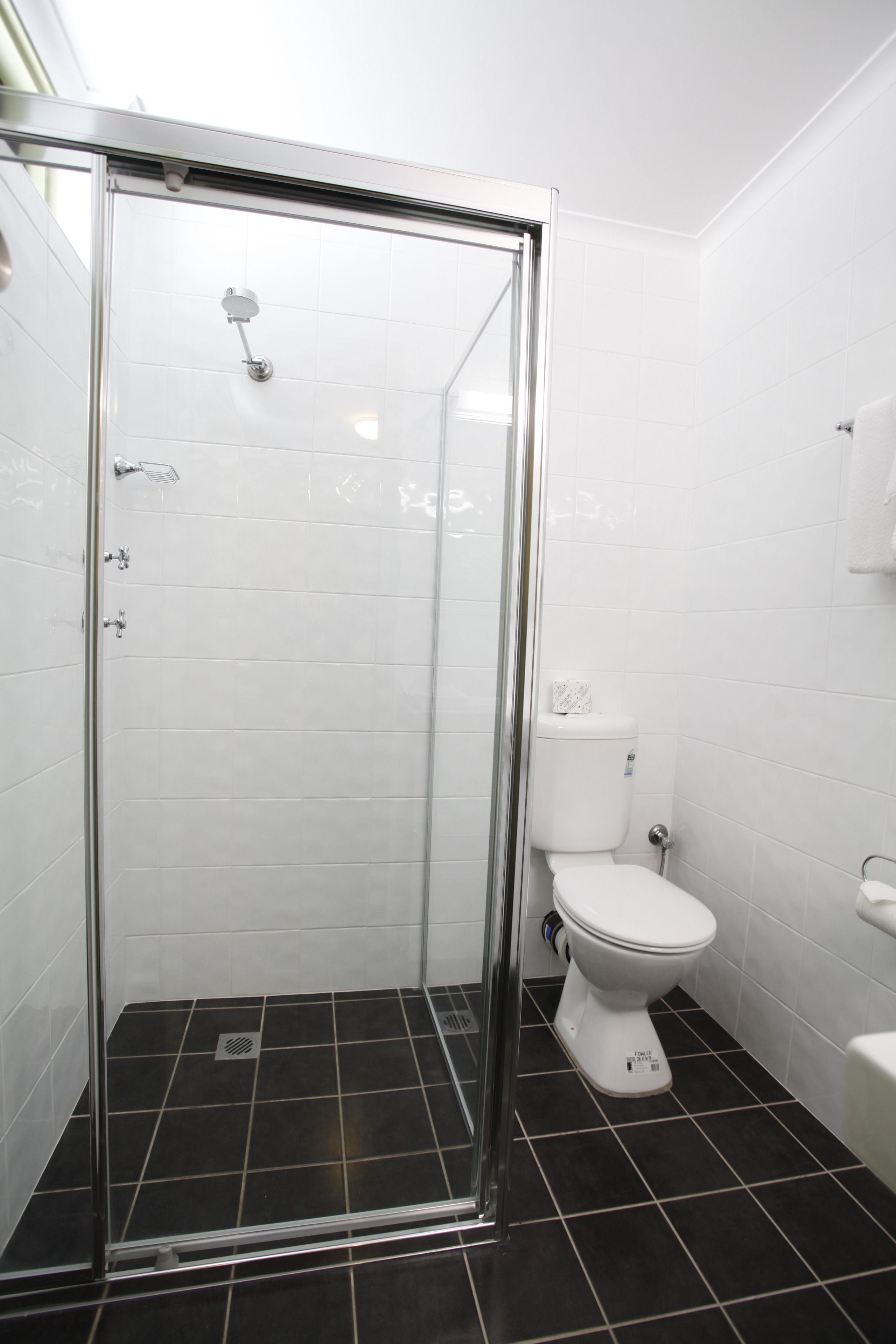 Un baño con ducha de vidrio, azulejos blancos y piso de baldosas negras.