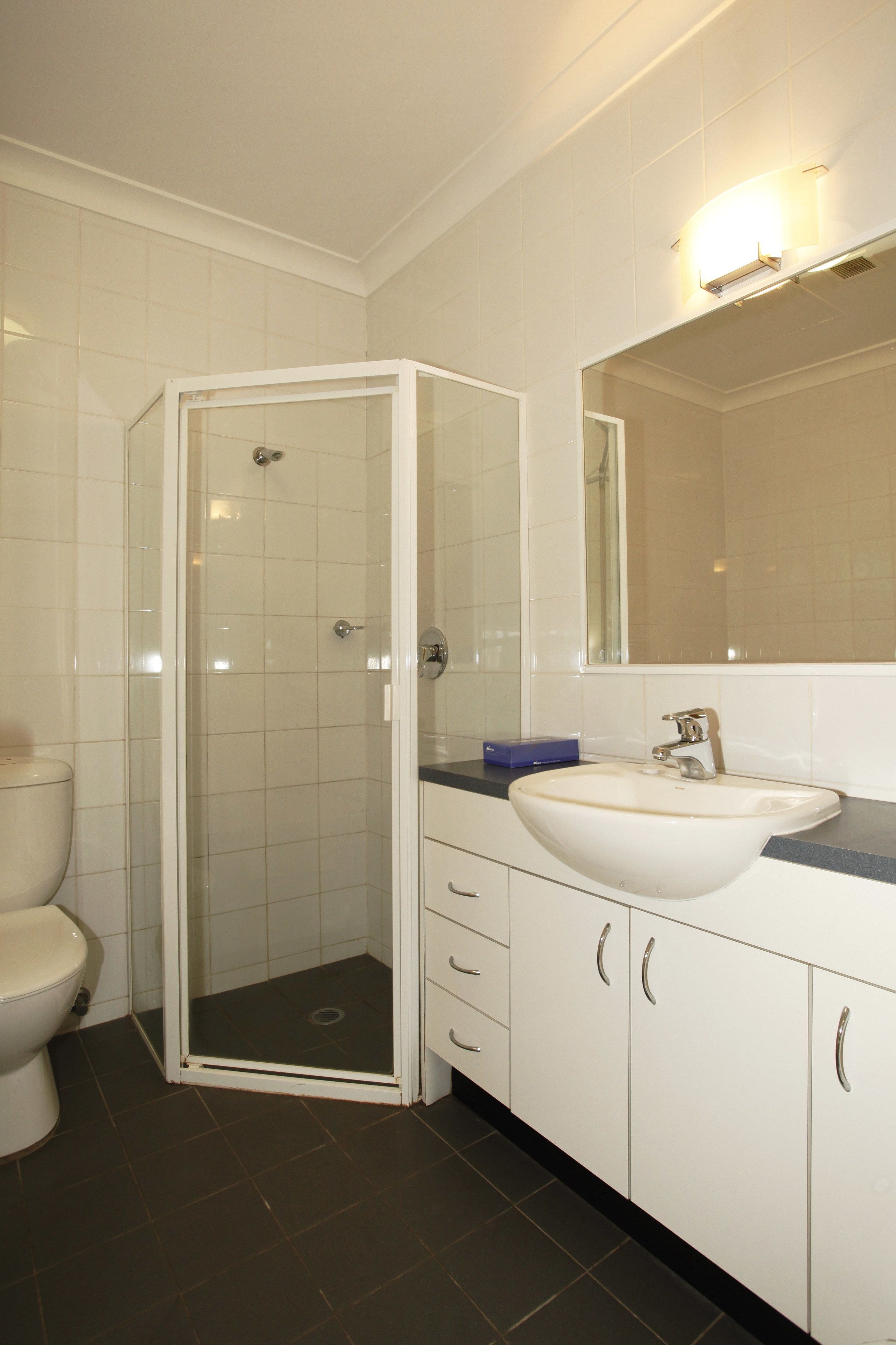 Un baño con ducha acristalada, lavamanos blanco y un espejo encima.