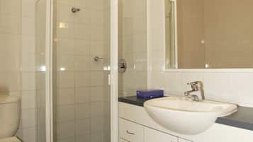 Un baño con ducha acristalada, lavamanos blanco y un espejo encima.