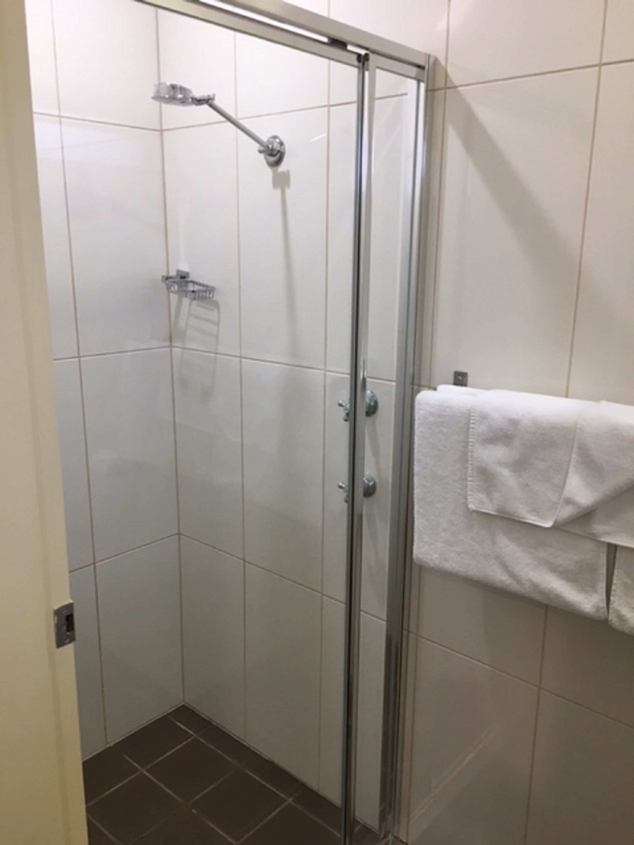 A glass-enclosed shower stall with a handheld showerhead, a towel rack with a towel, and tiled walls.