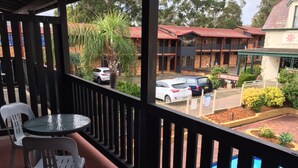 A balcony with two chairs and a table, overlooking a parking area with cars and a building with a red roof. - Maclin Lodge Motel (Campbelltown)