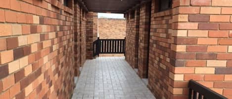 A covered corridor with brick walls and a tiled floor, leading to an open area.