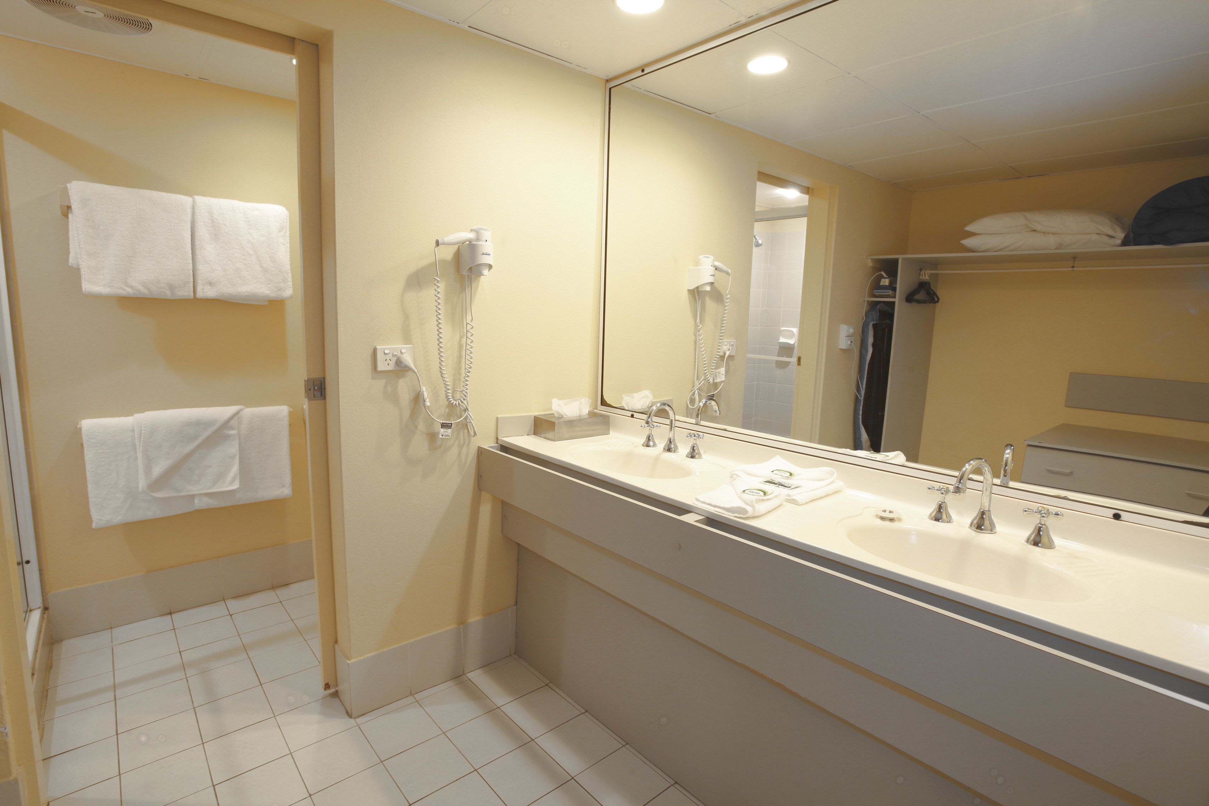 A hotel bathroom with a large mirror, two sinks, and a shower.