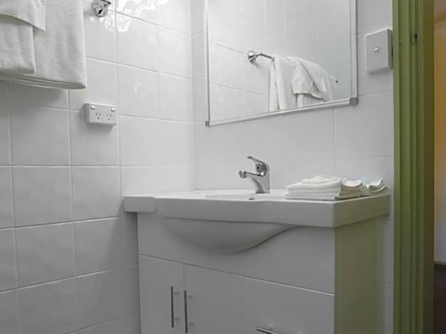 A bathroom with white tiles, a sink, a mirror, a towel rack, and a trash bin.
