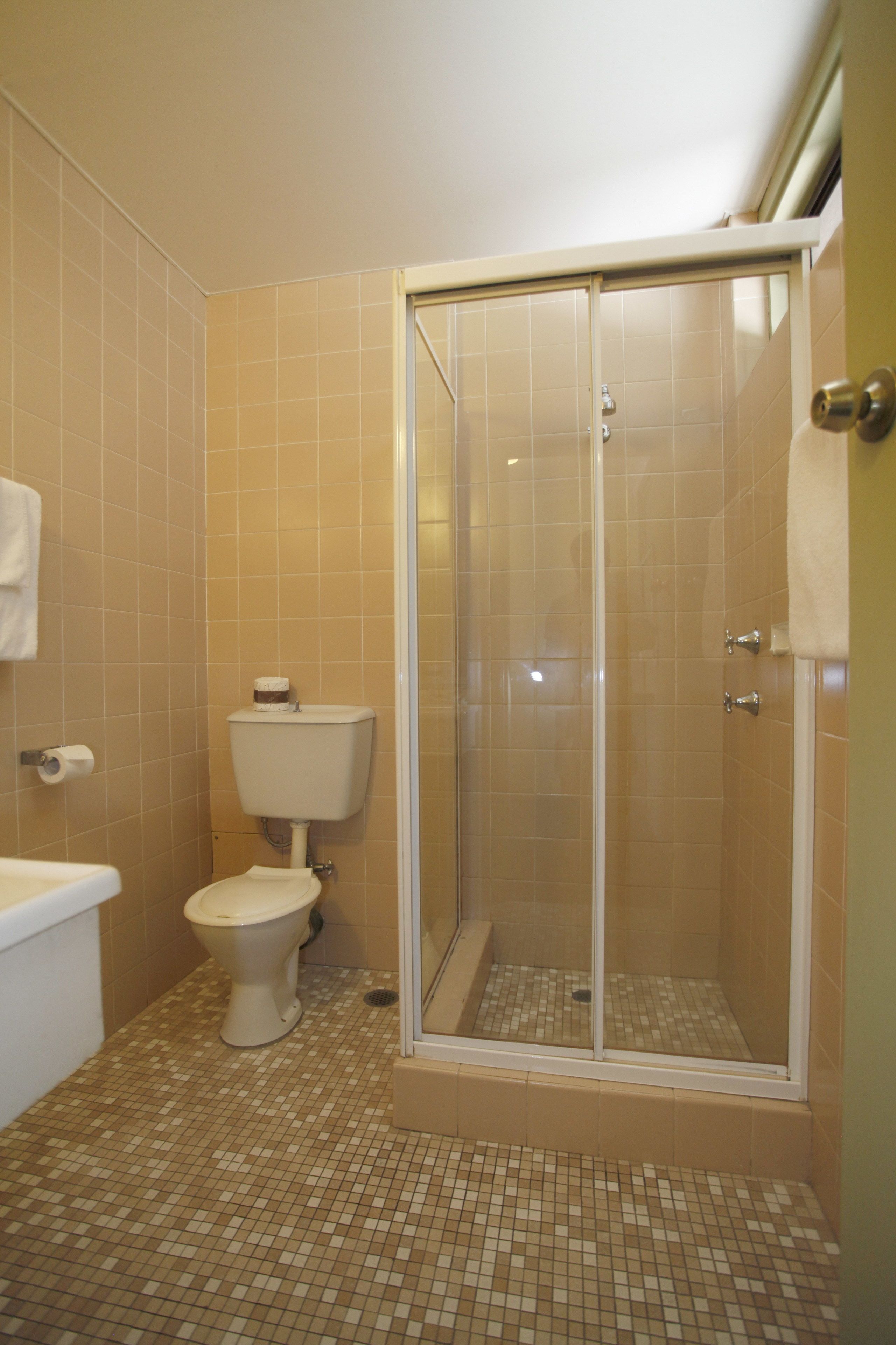 A bathroom with a toilet, a shower with a glass door, and tiled flooring.