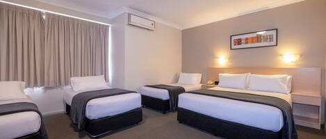 Habitación de hotel con cuatro camas individuales, un ventanal grande con cortinas, un equipo de aire acondicionado, una obra de arte colgada en la pared y dos apliques.
