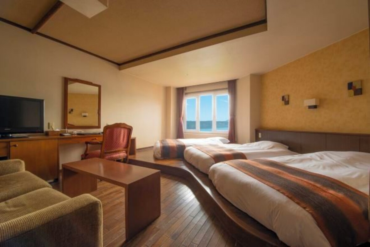 A hotel room with a large bed, a desk, a chair, a television, and a window with a view of the sea.