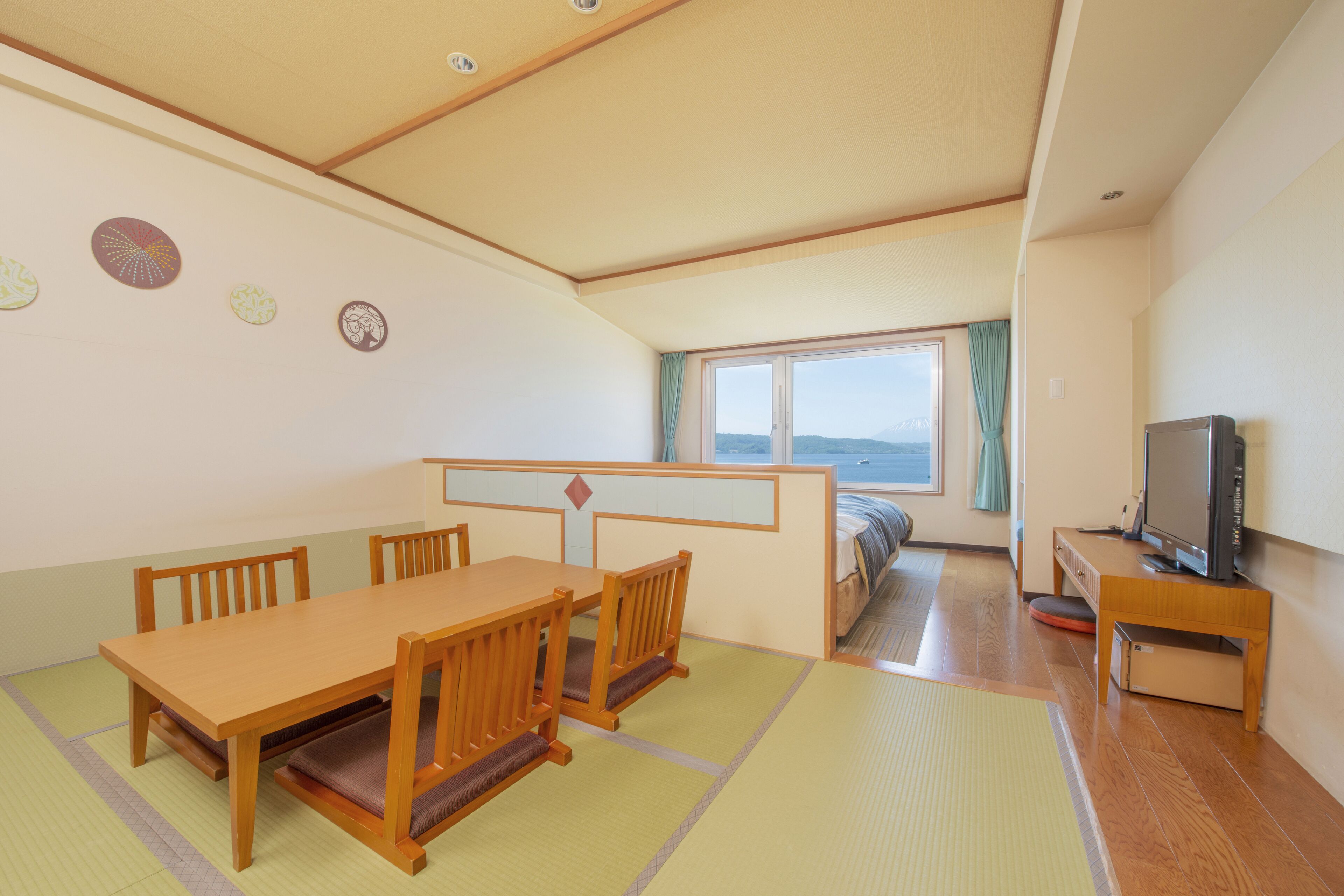 A traditional Japanese-style room with tatami mat flooring, a wooden dining table, and a television on a wooden stand.