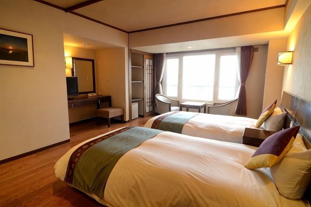 Une chambre d’hôtel avec deux lits, un bureau, une chaise, une petite table et une fenêtre avec des rideaux.