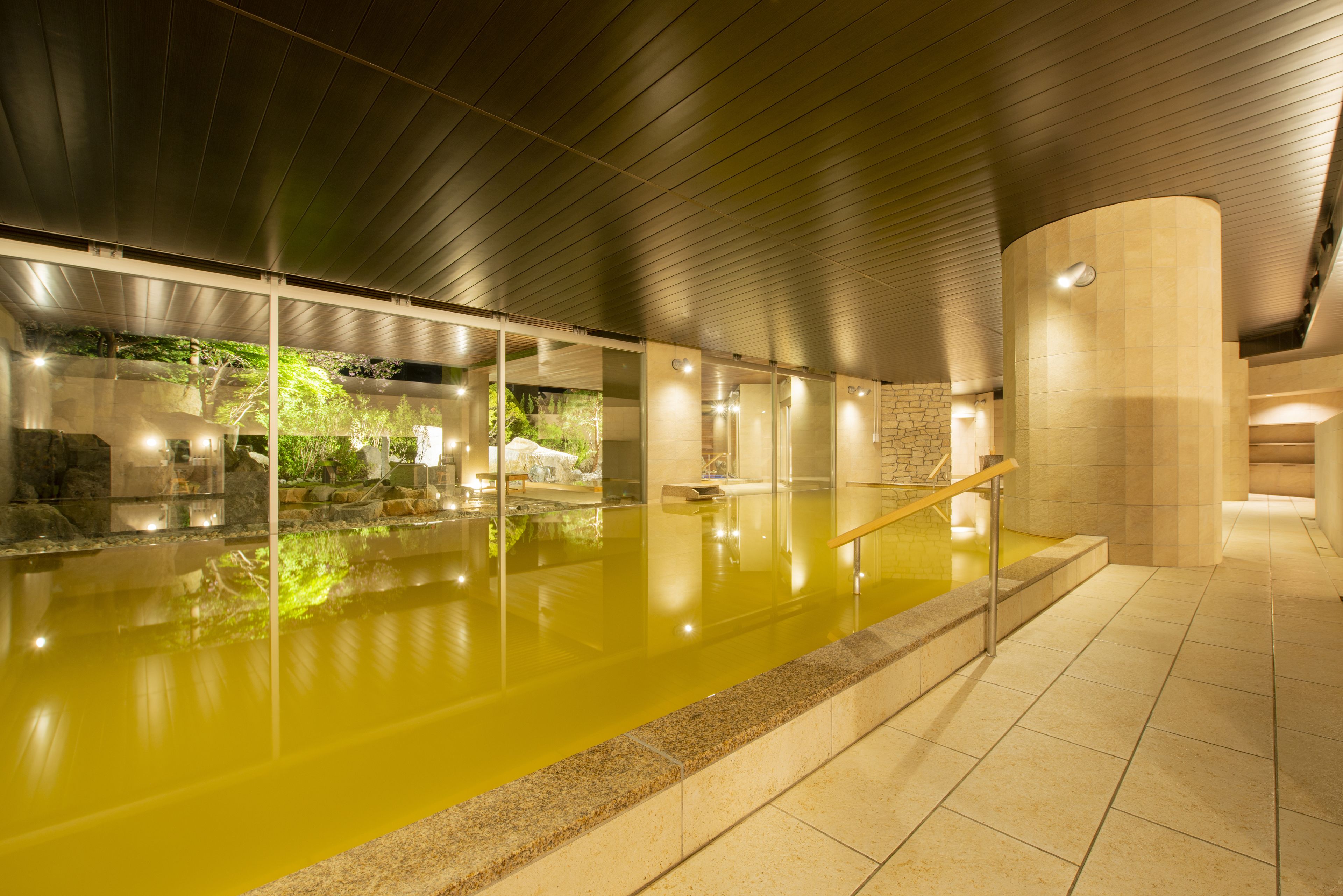 An indoor swimming pool with clear water, surrounded by stone walls and a wooden ceiling.