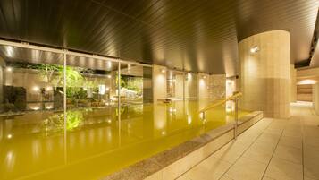 An indoor swimming pool with clear water, surrounded by stone walls and a wooden ceiling.