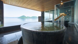 Een wellnessruimte met een groot houten bad, een houten trap en uitzicht op zee.