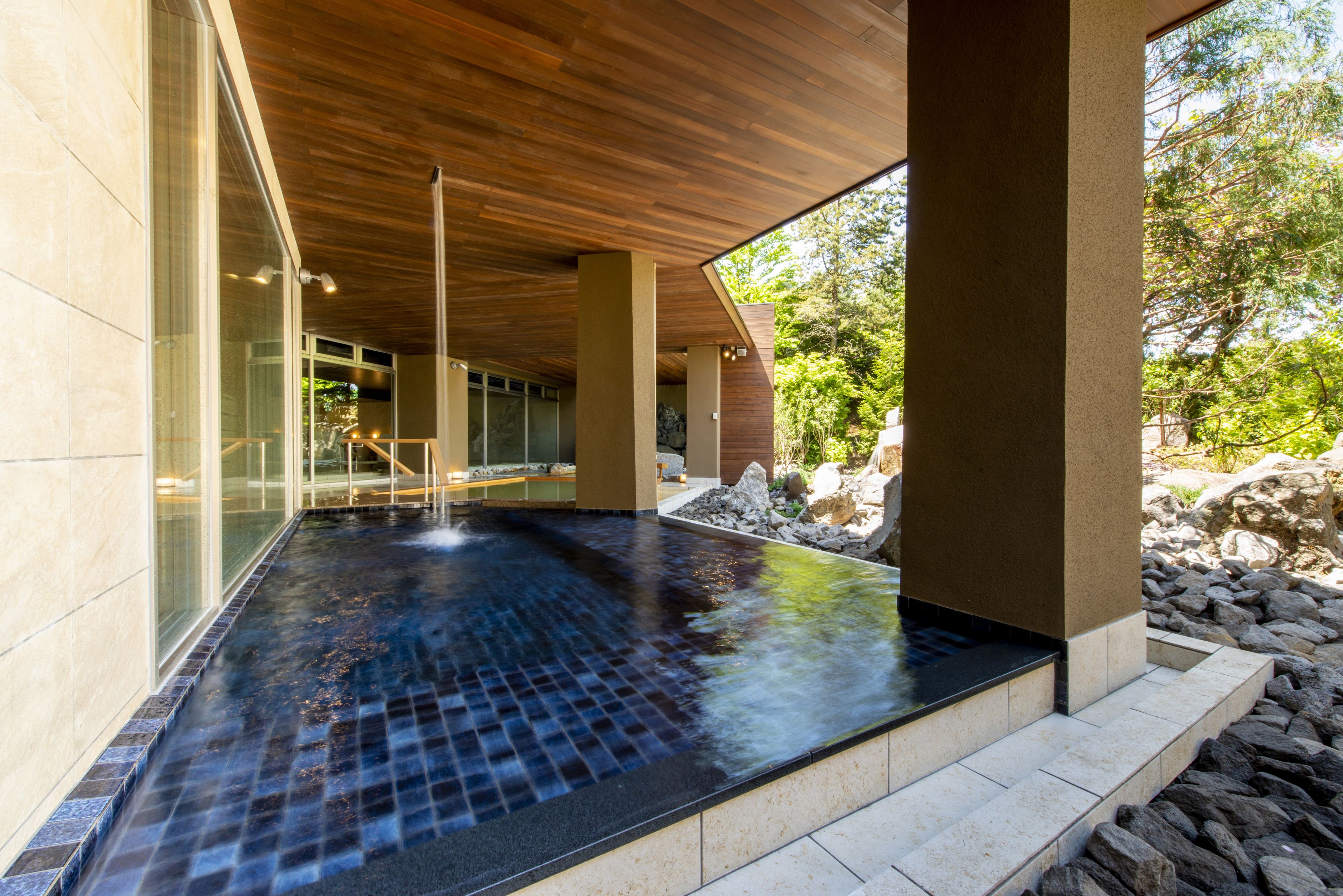 Un espacio moderno de spa con suelo de baldosas negras, techo de madera y amplios ventanales.