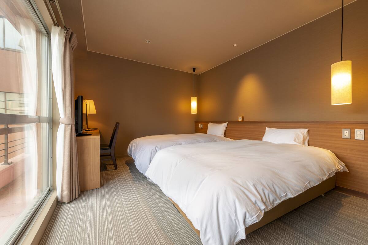 Une chambre d’hôtel avec un grand lit, un bureau, une chaise et une fenêtre avec des rideaux.