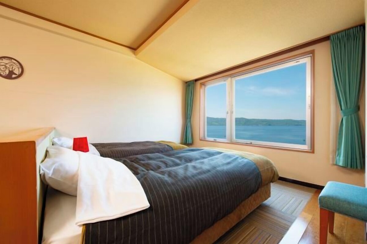 Une chambre à coucher avec un lit, une fenêtre avec des rideaux, un plancher en bois et une vue sur la mer.