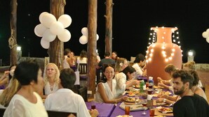 An outdoor dining area with tables and chairs, a large decorative vase centerpiece, and white balloons.