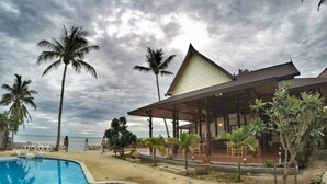 A resort with a swimming pool, palm trees, and a covered outdoor area with seating.