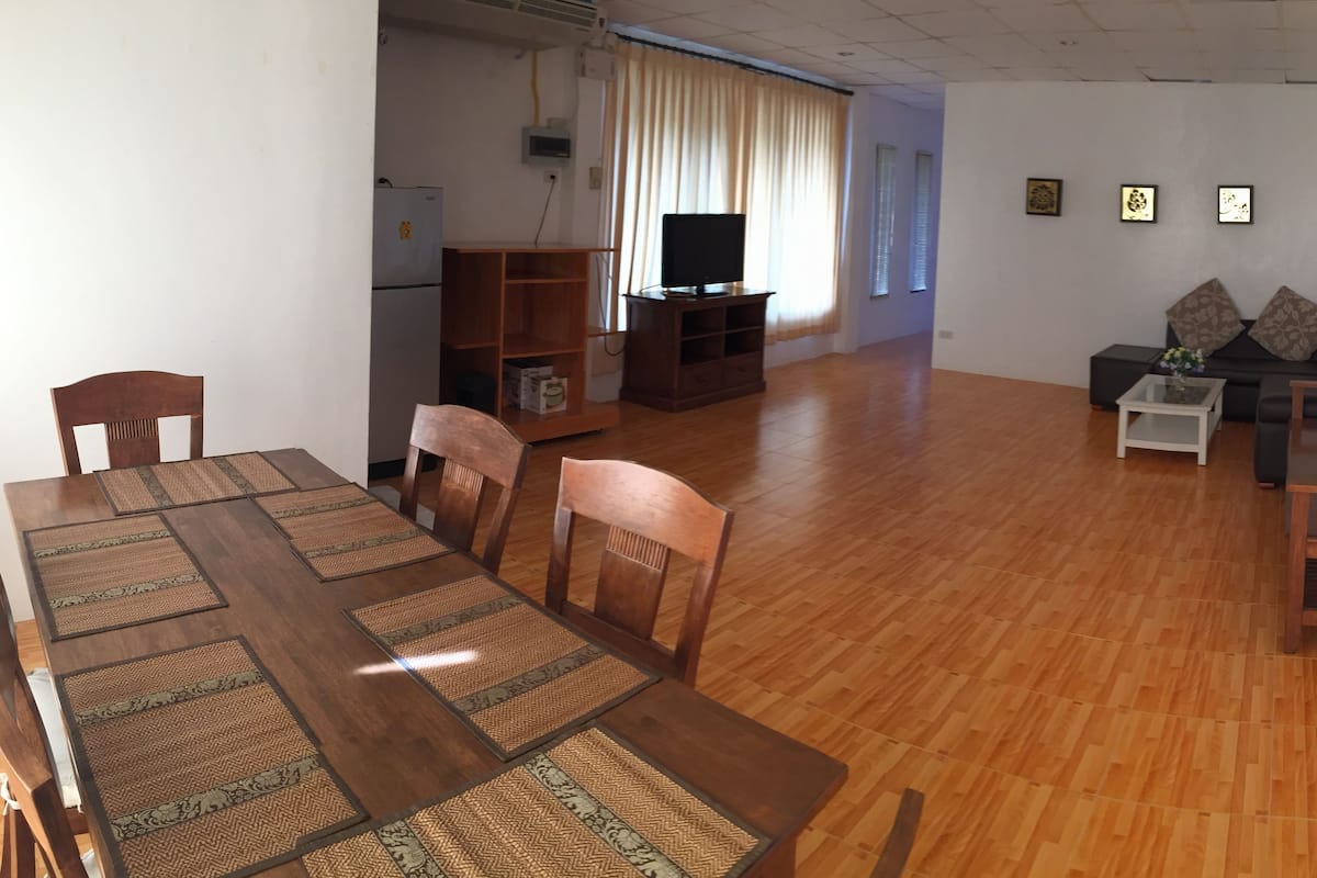Ein geräumiger Wohnbereich mit einem Holzesstisch, Stühlen, einer Couch und einem Fernseher.