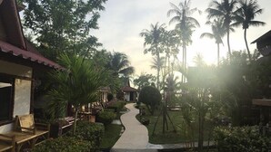 A pathway leading to a building with a tiled roof, surrounded by lush greenery and palm trees.