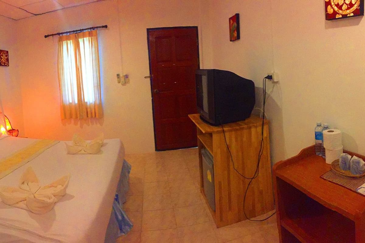 Ein Hotelzimmer mit einem Bett, einem Fernseher auf einem Holzboden, einer Tür und einem kleinen Tisch mit Pflegeprodukten.